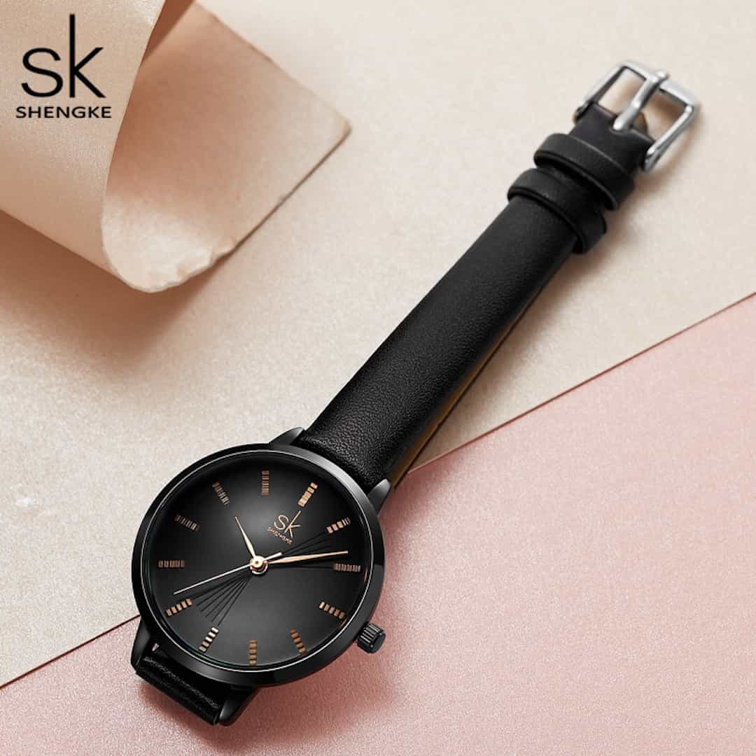 Ženska ročna ura SK Shengke Graceful Black položena na elegantno ozadje.