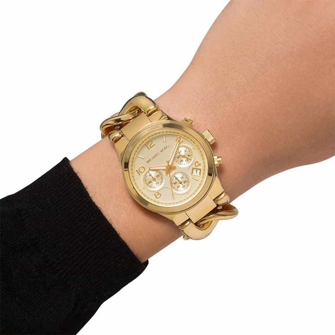 Ženska nosi zlato uro Michael Kors Runway Twist MK3131 na zapestju